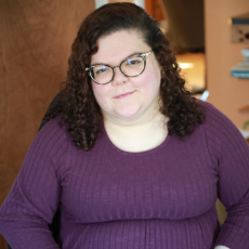 Emily Ladau in a purple sweater and glasses smiling at the camera.
