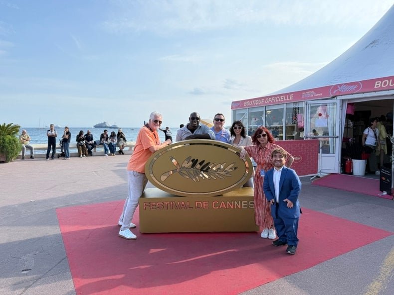Group of five adults posing in front of the Cannes Film Festival logo at a scenic outdoor venue.