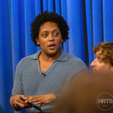 Jerome Core engaged in a conversation at an HRTS panel event, with one person holding a microphone. Review AI-generated content for inaccuracies, biases or offensive material.