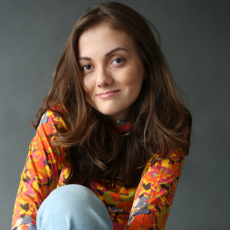 Tal Anderson wearing a colorful floral shirt and jeans, sitting and smiling at the camera with a subtle expression.