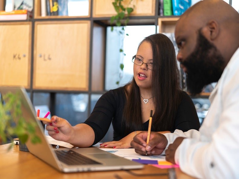 a young woman and man working together on a laptop computer