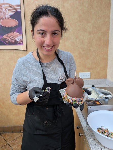 Makena wearing a black apron and holding a chocolate covered apple. 