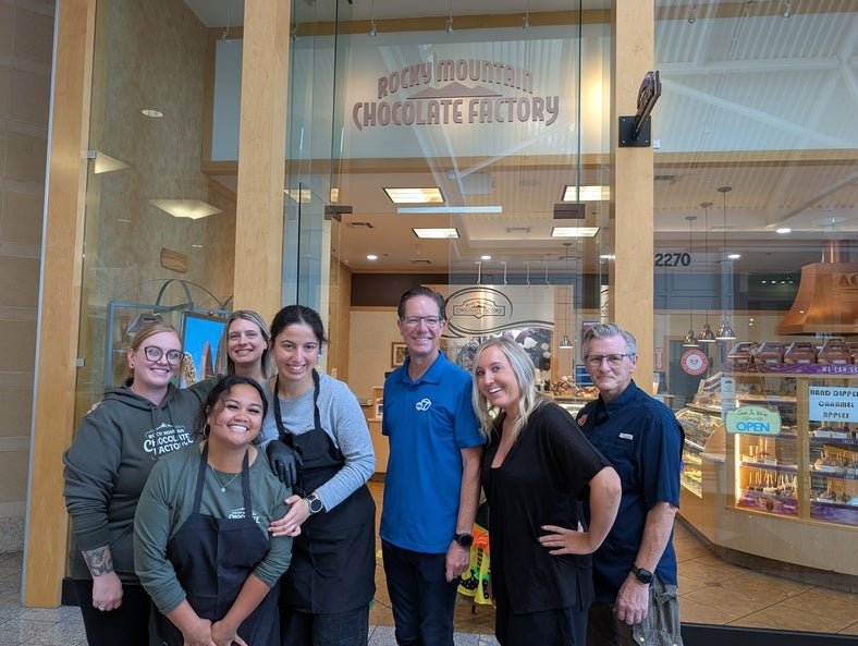 Seven individuals standing in front of Rocky Mountain Chocolate Factory. 