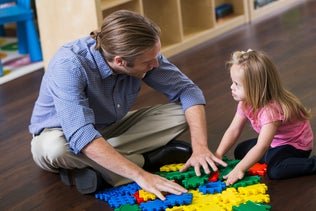 Adult and child playing with colorful building blocks on the floor.