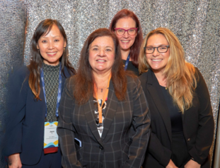 (L to R) Dr. Joyce Tu, Dr. Paula Pompa-Craven, Jennie Myhra, and Alyssa Kavner standing in front of a sparkly backdrop.