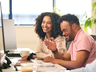 man with disability sitting next to woman in front of computer
