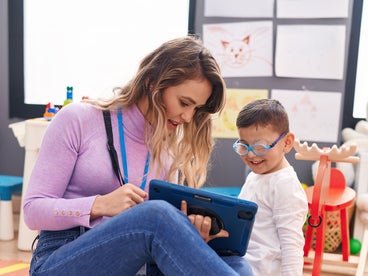 adult woman helping young boy with glasses use a tablet