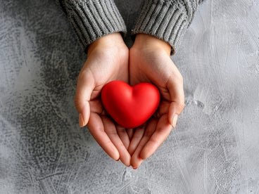 Hands holding a heart shaped red rock