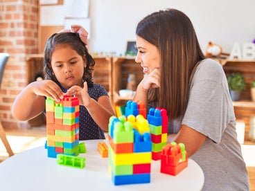 young girl stacking blocks next to adult woman