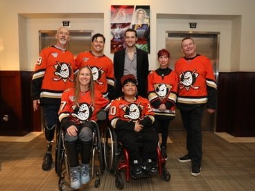 A group photo of seven individuals wearing Anaheim Ducks hockey jerseys.