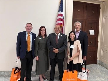 Group of five individuals posing in a hallway with an American flag, outside an office labeled "Member of Congress." 