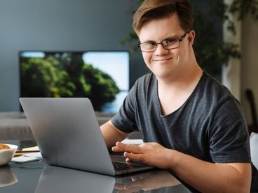 a young man sitting at the table using a laptop smiling
