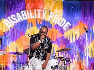 MC Down on stage rapping in front of a colorful fringe brakcdrop that says "disability pride." 