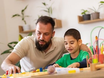 An adult and a child are engaged in an activity with colorful building blocks at a table filled with art supplies.