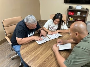 William and Jehada sitting with Life Skills Coach at a table studying for a permit test. 