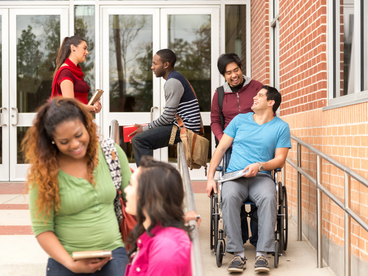 Six students outside a building engaged in multiple conversations. 