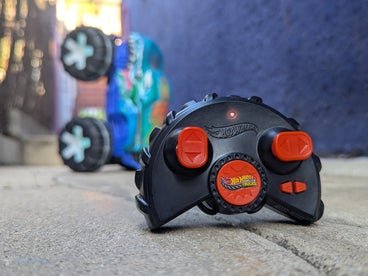 A hot wheel toy car on the ground titled and the forefront the RC controller. 