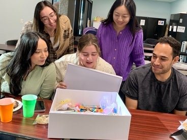 A group of five individuals eagerly and happily opening a Kindness Kit. 