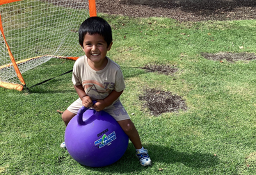 Jameson bouncing on a purple ball in a backyard setting. 