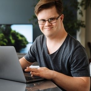 a young man sitting at the table using a laptop smiling