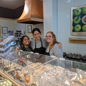 Three individuals in a pastry shop behind the counter. 