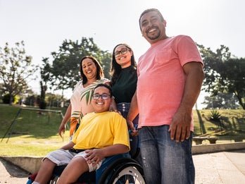 Family of four standing in front of a park one child is in a wheelchair
