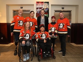 A group photo of seven individuals wearing Anaheim Ducks hockey jerseys.