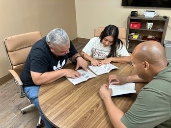 William and Jehada sitting with Life Skills Coach at a table studying for a permit test. 