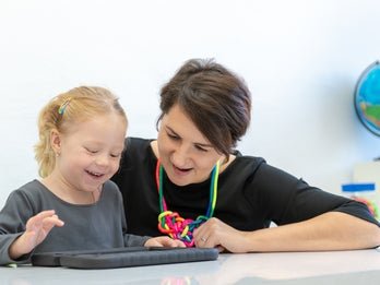 A woman and a child sitting in a classroom using an AAC device. 