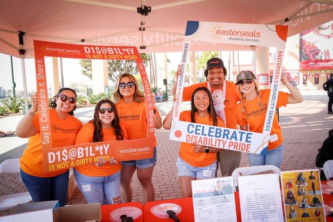 Staff members at the Angels game wearing orange Easterseals shirts and holding up frames that say "Disability is Not a Dirty Word" 