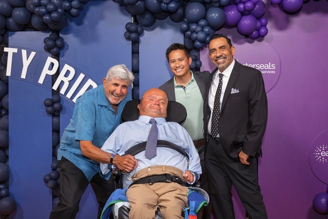 A participant poses along with ADS staff members in front of a purple and blue backdrop 