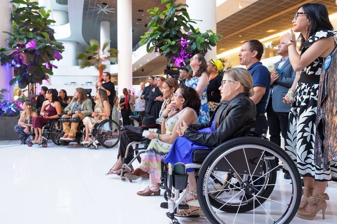 Guest at the event, some using wheelchairs and others standing, look on to the stage during the speeches 