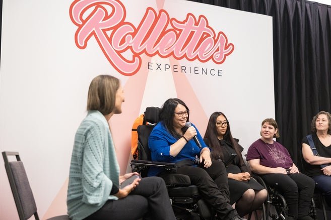 Easterseals participants Betty and Lora on stage speaking on a panel in front of a Rollettes back drop 