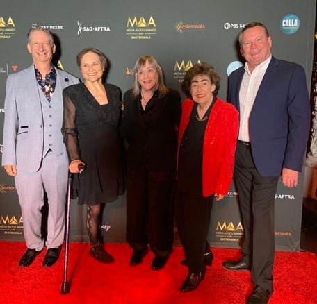 Five individuals posing together at the Media Access Awards event. They are smiling and dressed in formal evening wear.