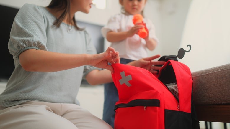 An adult and a child packing a red emergency backpack with supplies.