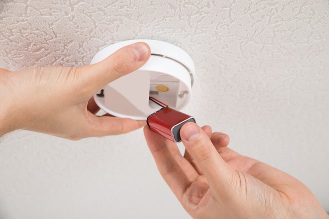 A person replacing a battery in a smoke detector on a ceiling.
