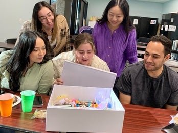 A group of five individuals eagerly and happily opening a Kindness Kit. 