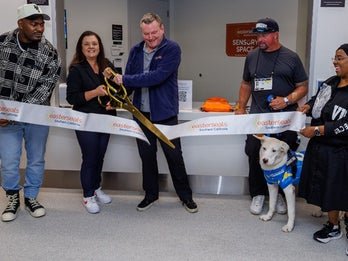 Five individuals and the Chargers pup cutting a ribbon in front of Guest Services. 